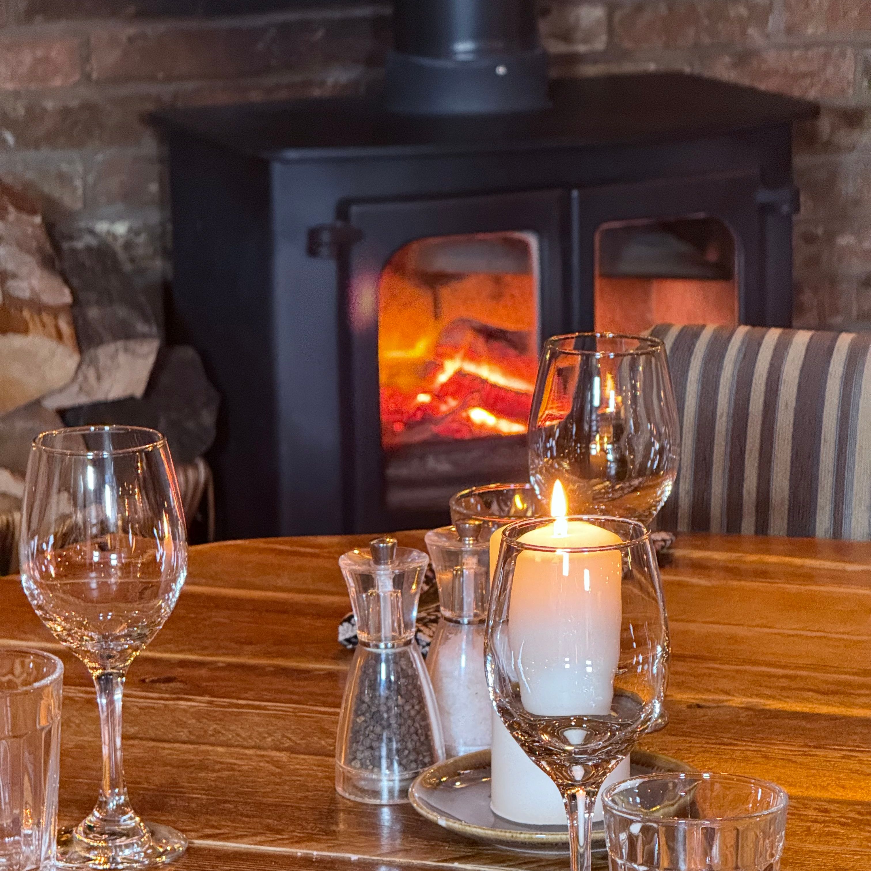 Cozy dining table with candle and glassware near a wood-burning stove