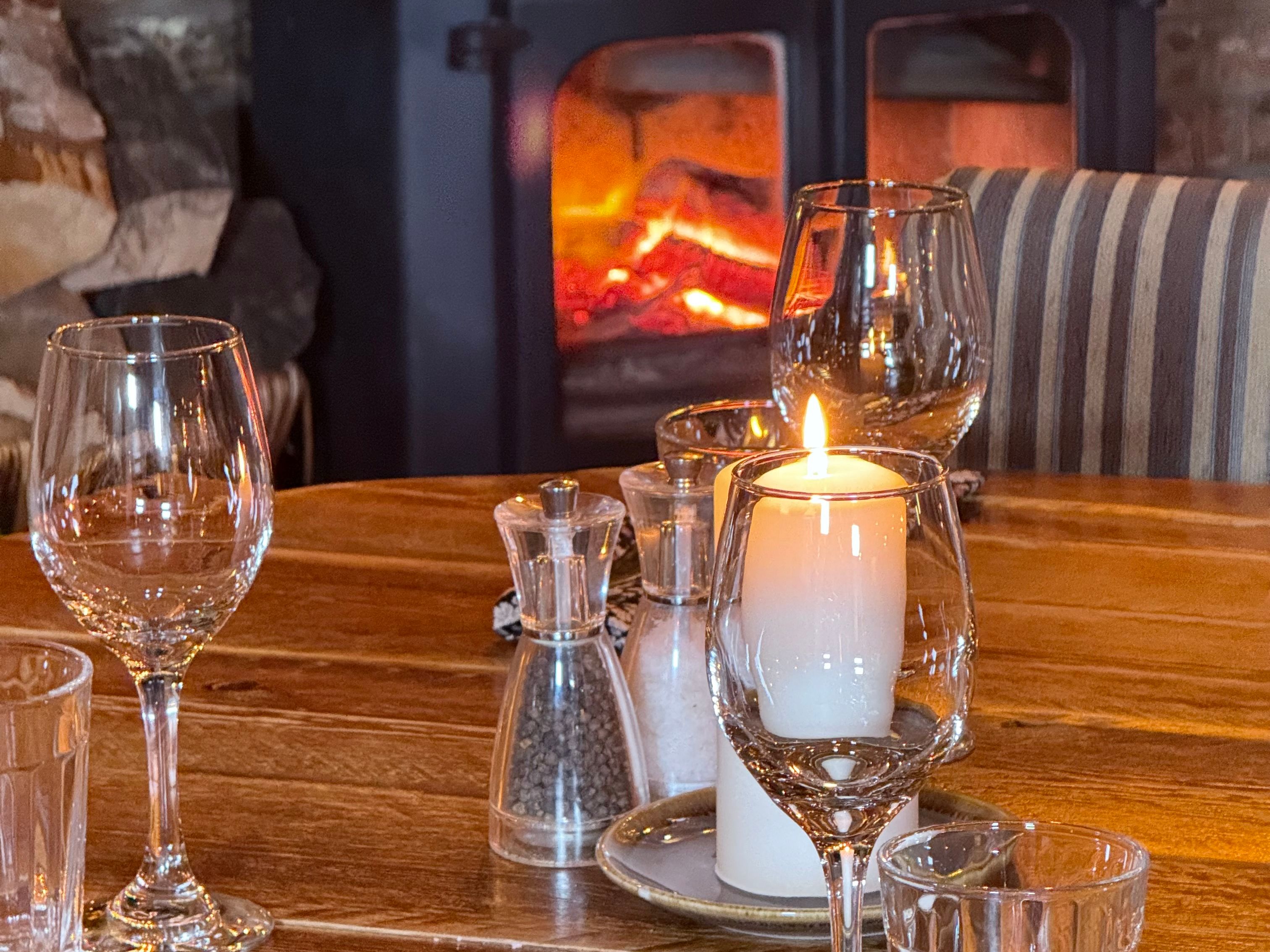 Cozy dining table with candle and glassware near a wood-burning stove
