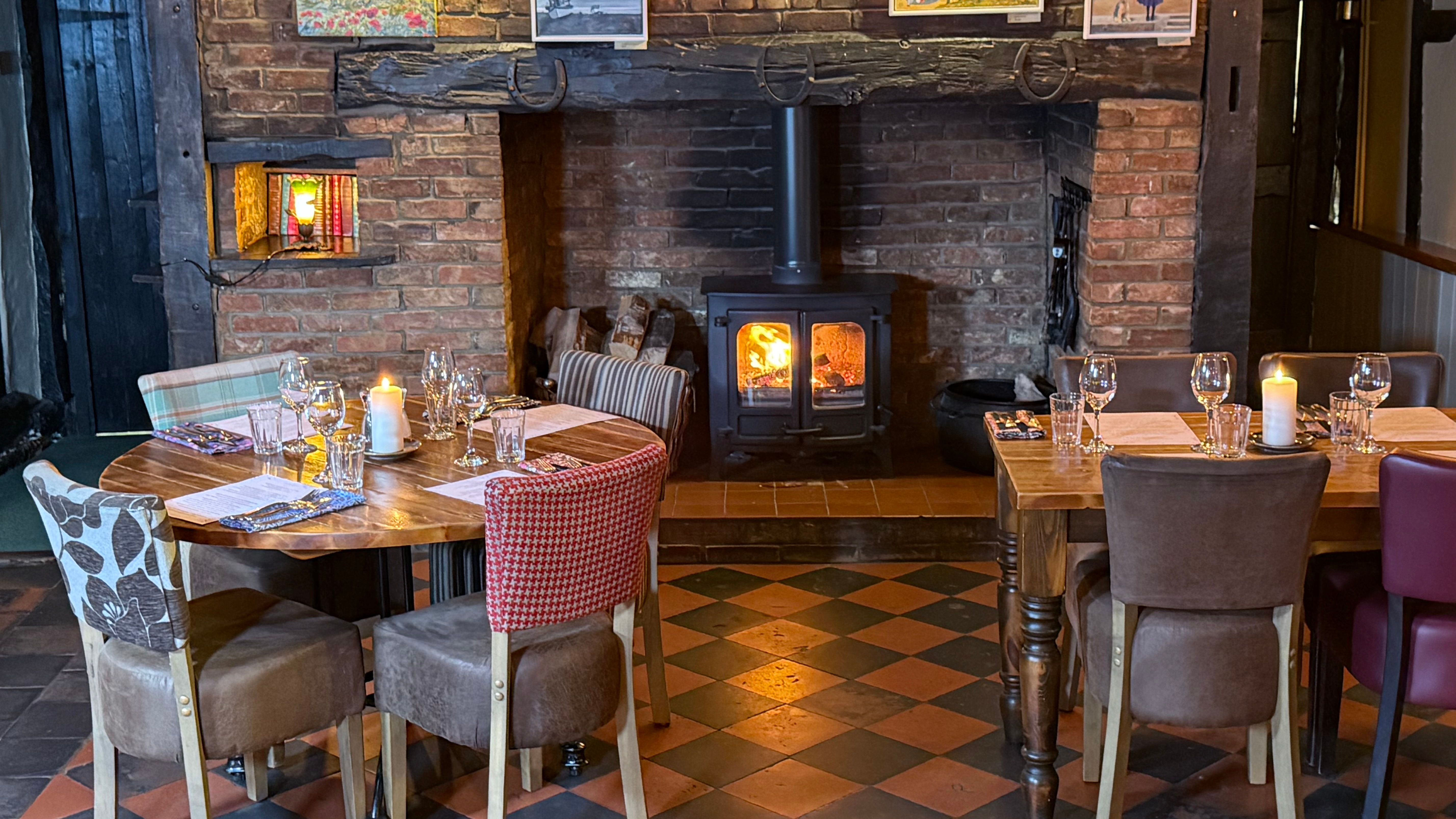 Cozy restaurant interior with a wood-burning stove, set tables, and artwork on a brick wall.