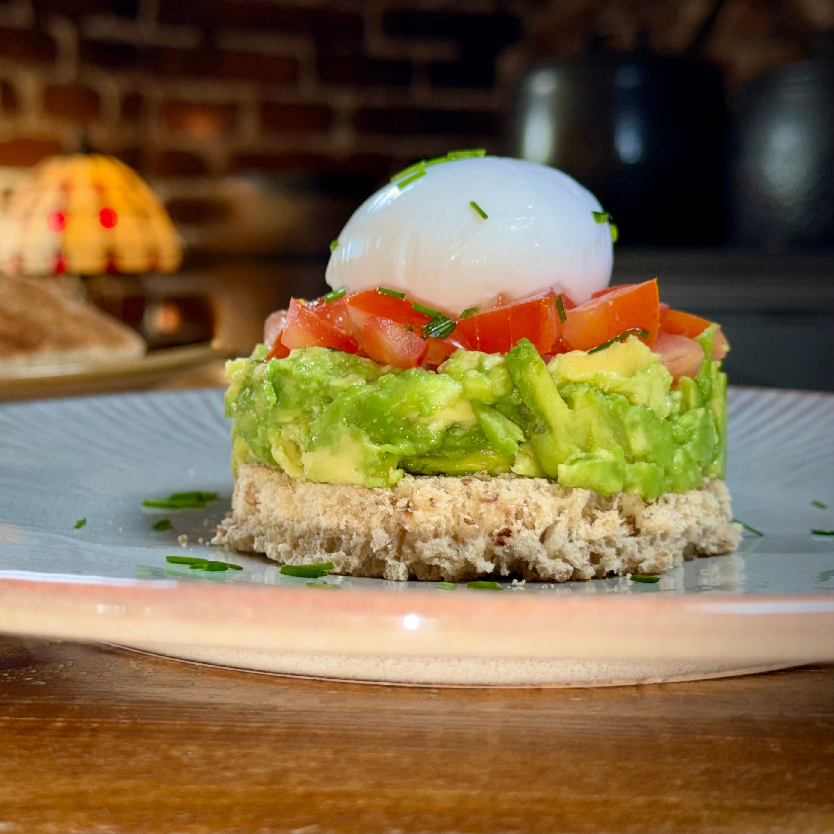 A breakfast plate with a stack of bread, mashed avocado, diced tomatoes, and a poached egg, with a glass of orange juice in the background.