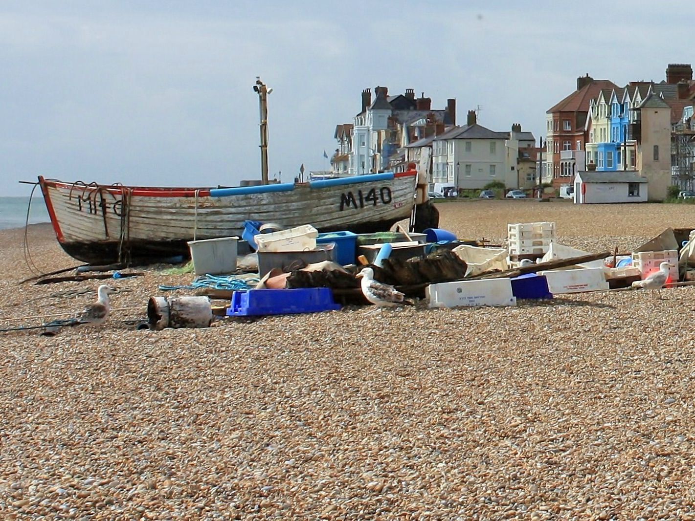 Fishing boat and fishing equipment on a pebble beach with seagulls and seaside houses in the background