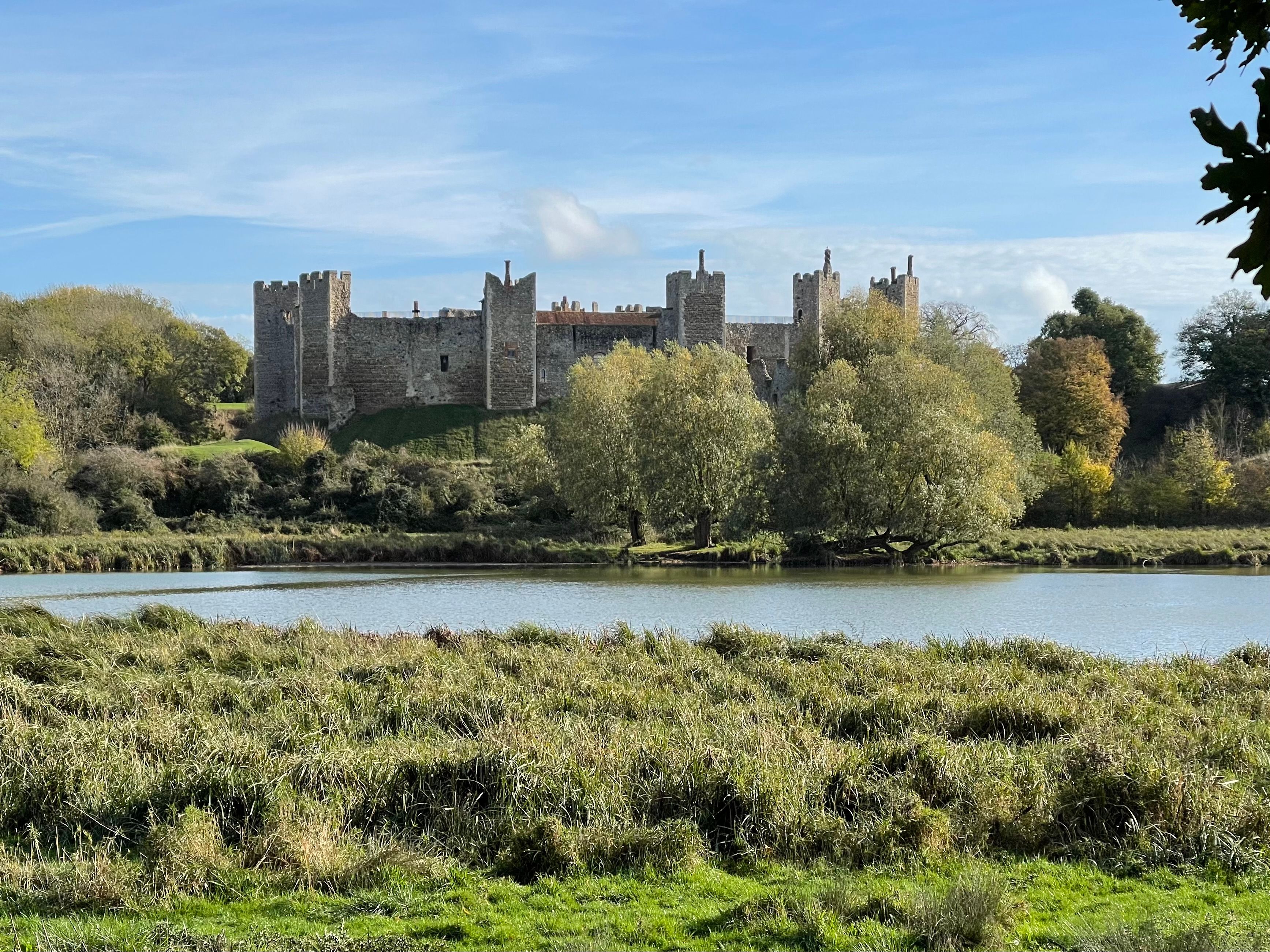 Historic stone castle with towers, surrounded by trees and a pond under a blue sky