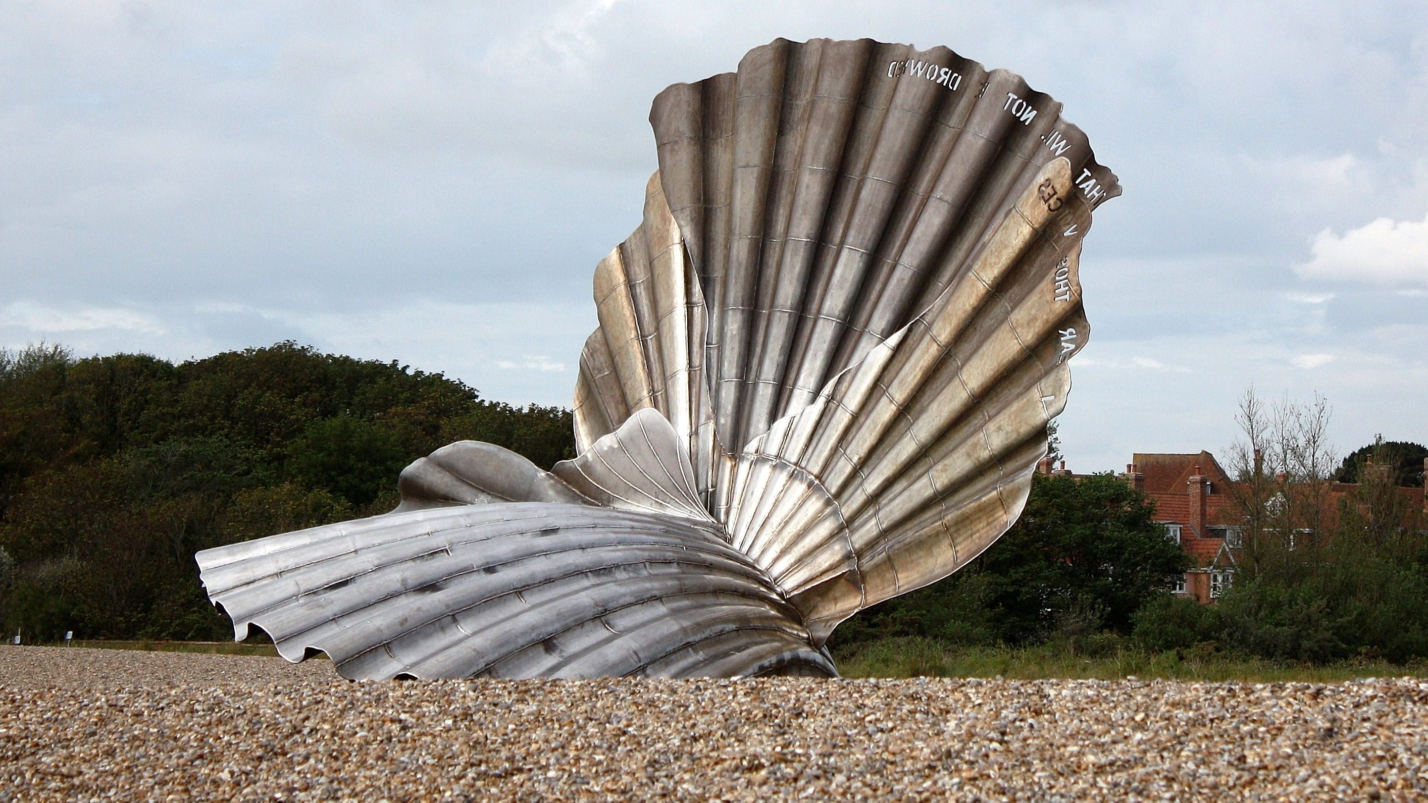 Large metallic scallop shell sculpture on a pebbled beach