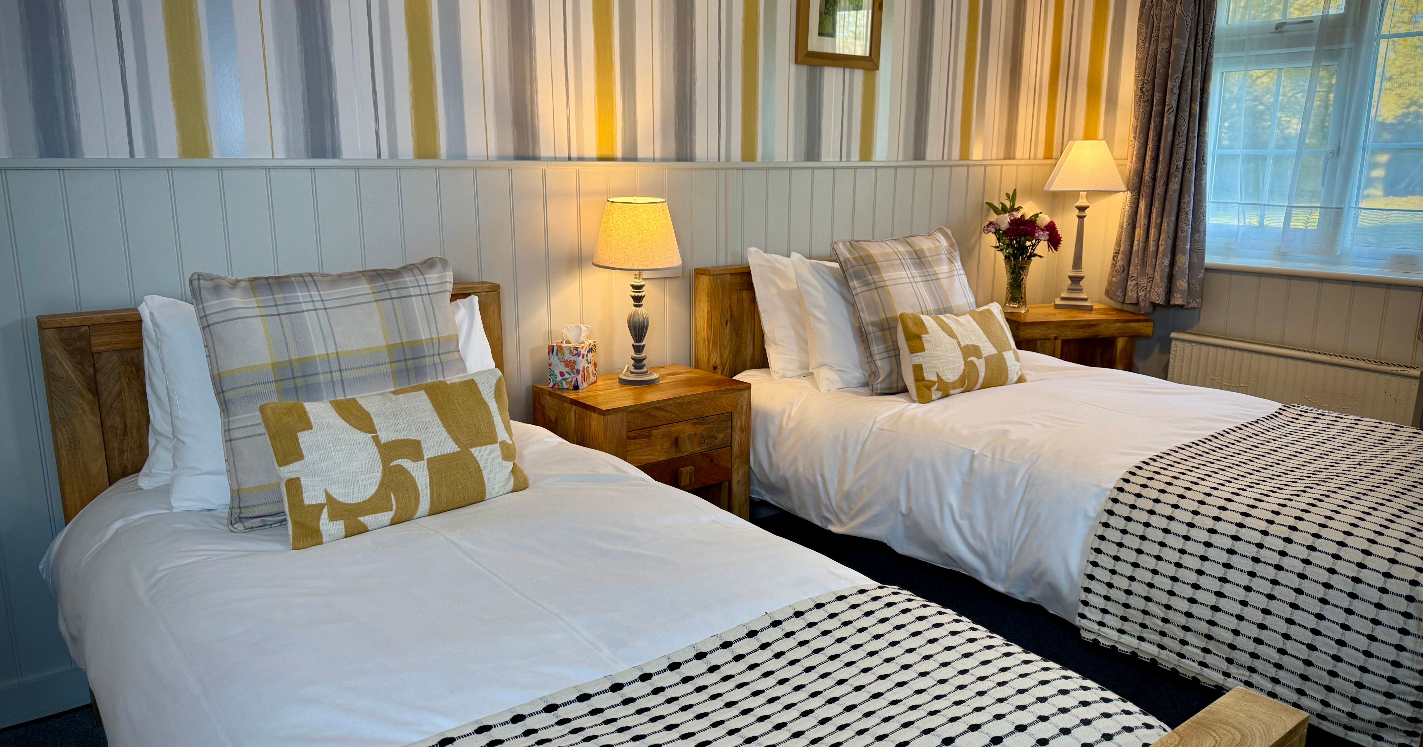 Cozy bedroom with two single beds, bedside tables, lamps, and patterned wallpaper