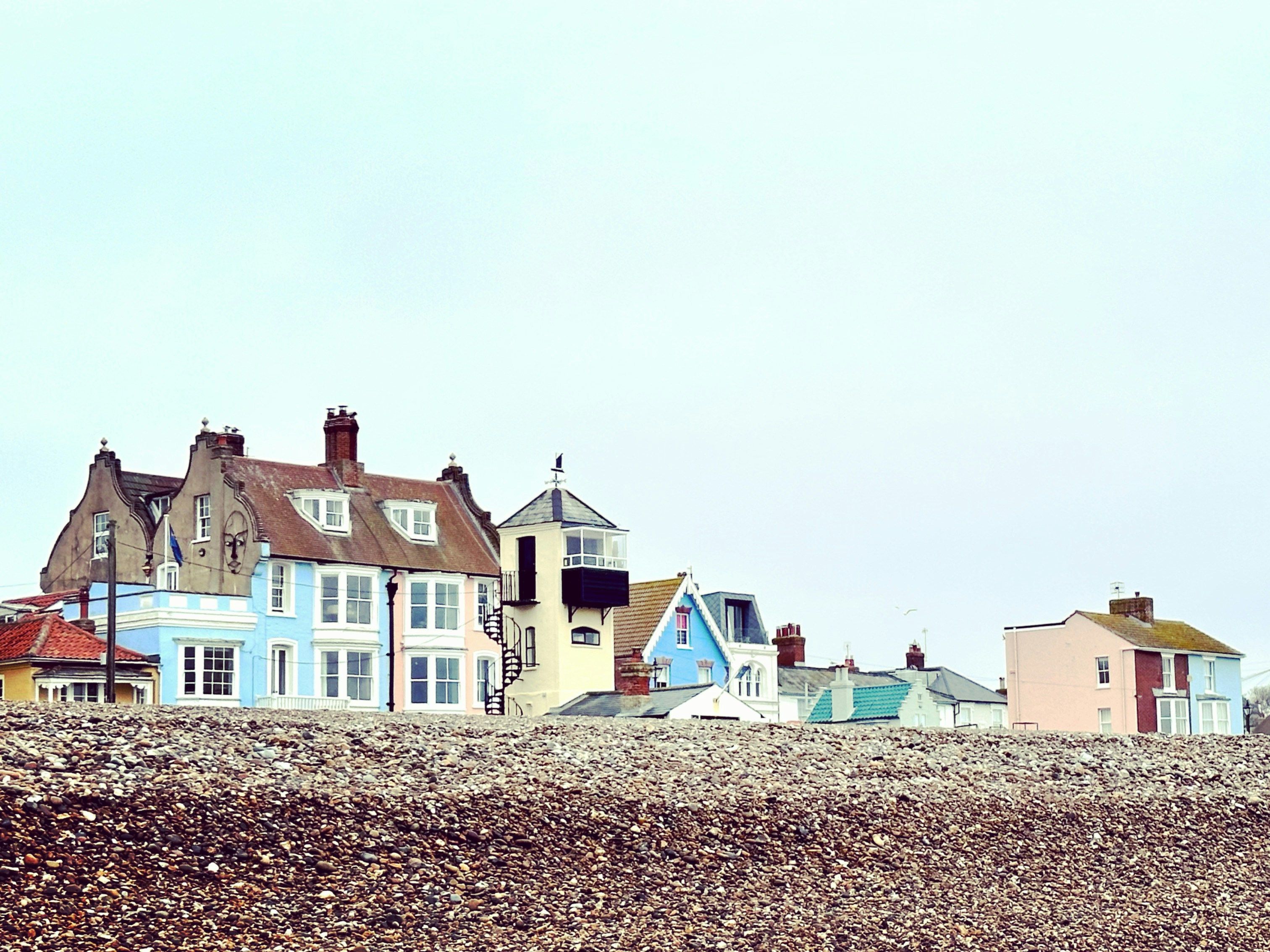 Colorful houses along the pebbled beachfront in Aldeburgh under an overcast sky.