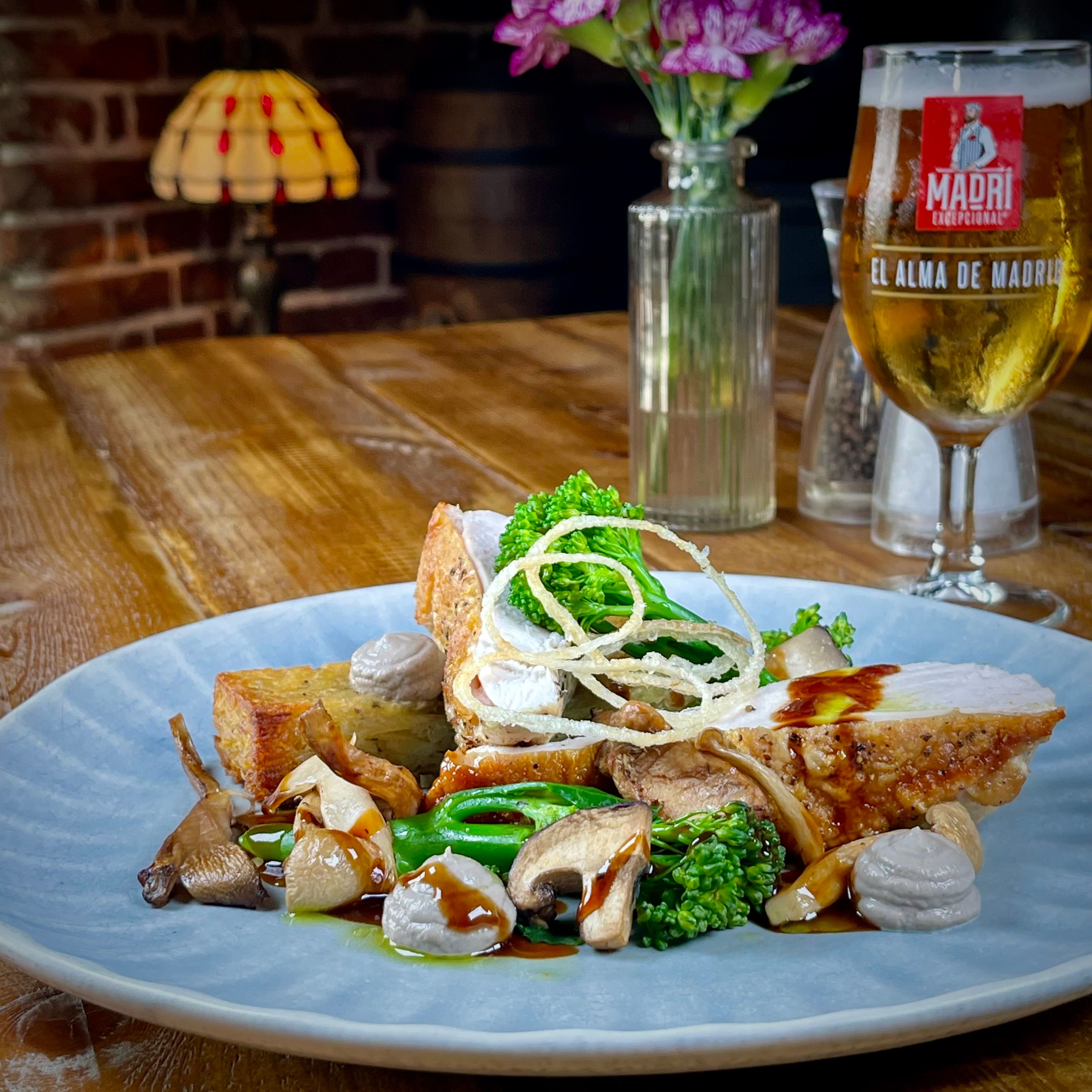 Gourmet chicken dish with vegetables, mushrooms, and crispy onions, served with a glass of beer on a wooden table