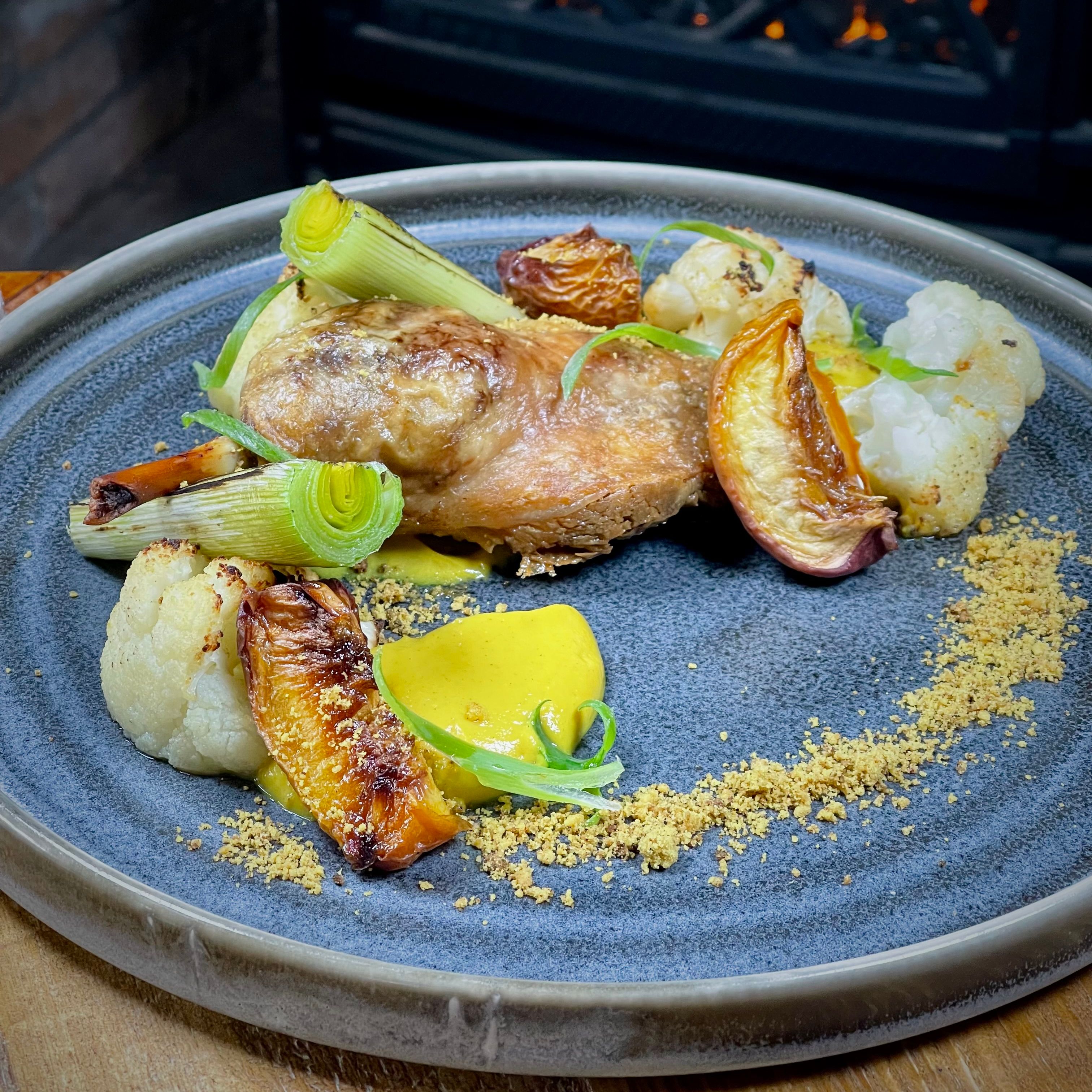 Gourmet chicken dish with vegetables and sauce artfully plated on a gray dish