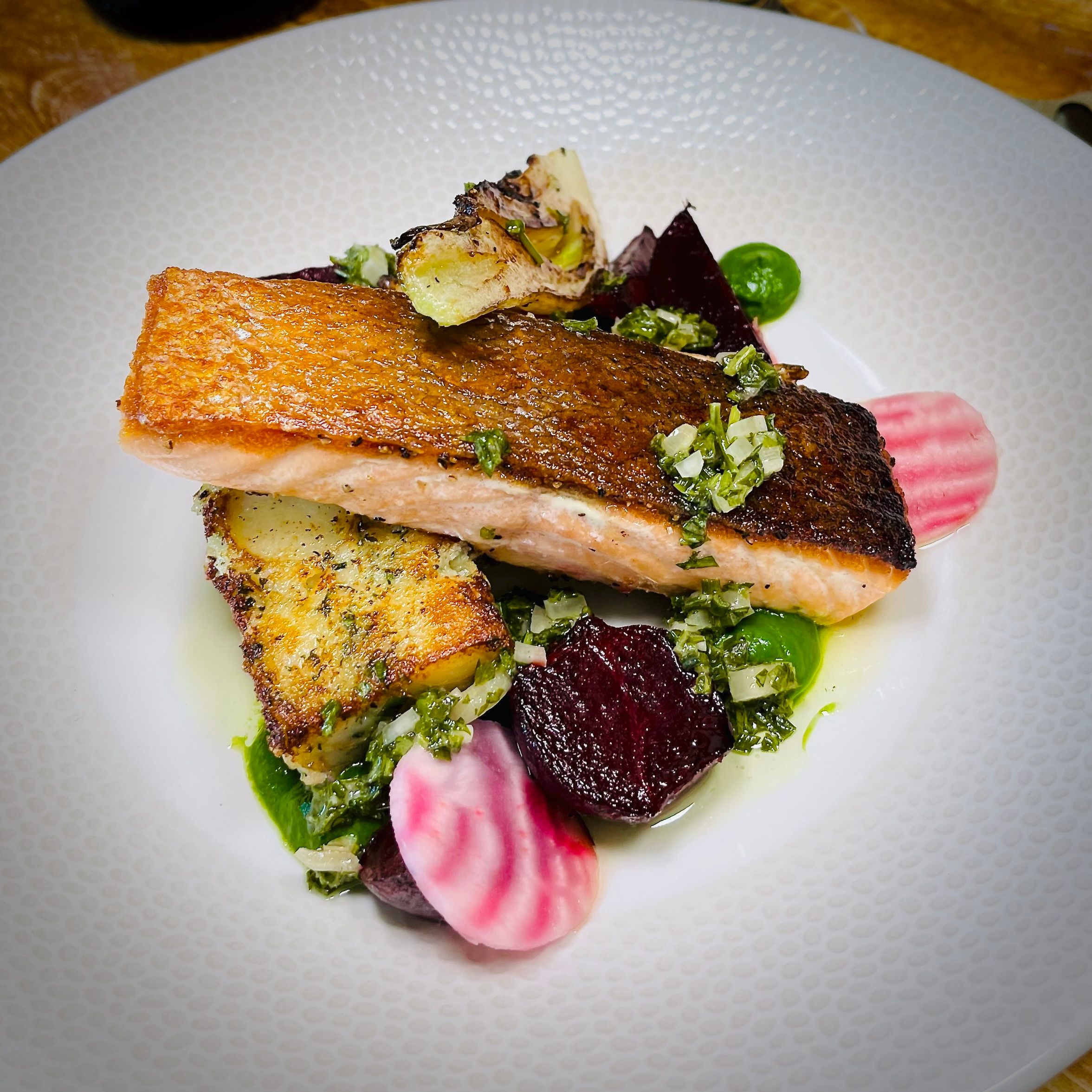 Plated salmon with crispy skin, accompanied by roasted vegetables and garnished with fresh herbs.