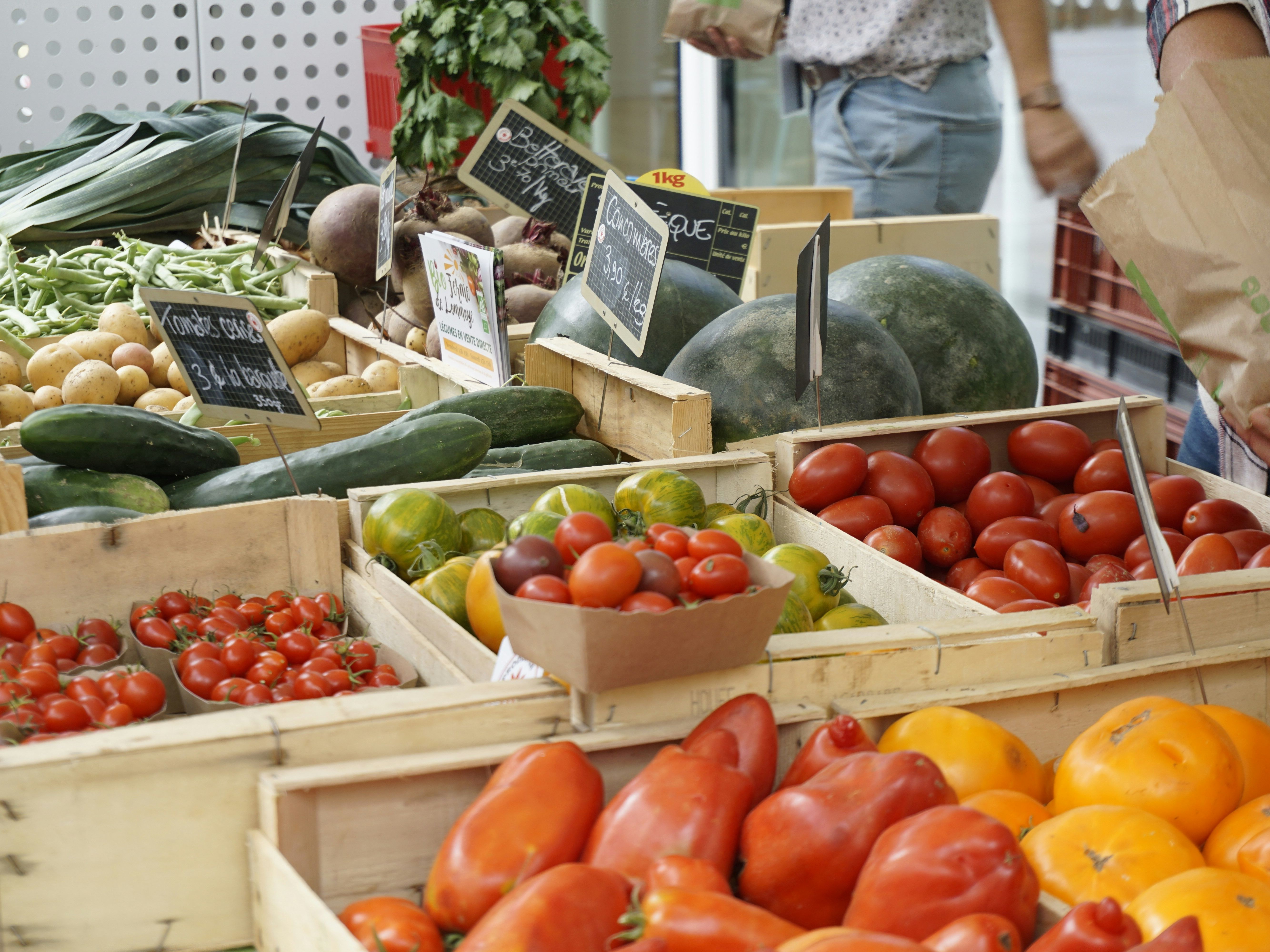 A farmers market stand displaying a variety of fresh vegetables including tomatoes, cucumbers, potatoes, green beans, and squash.