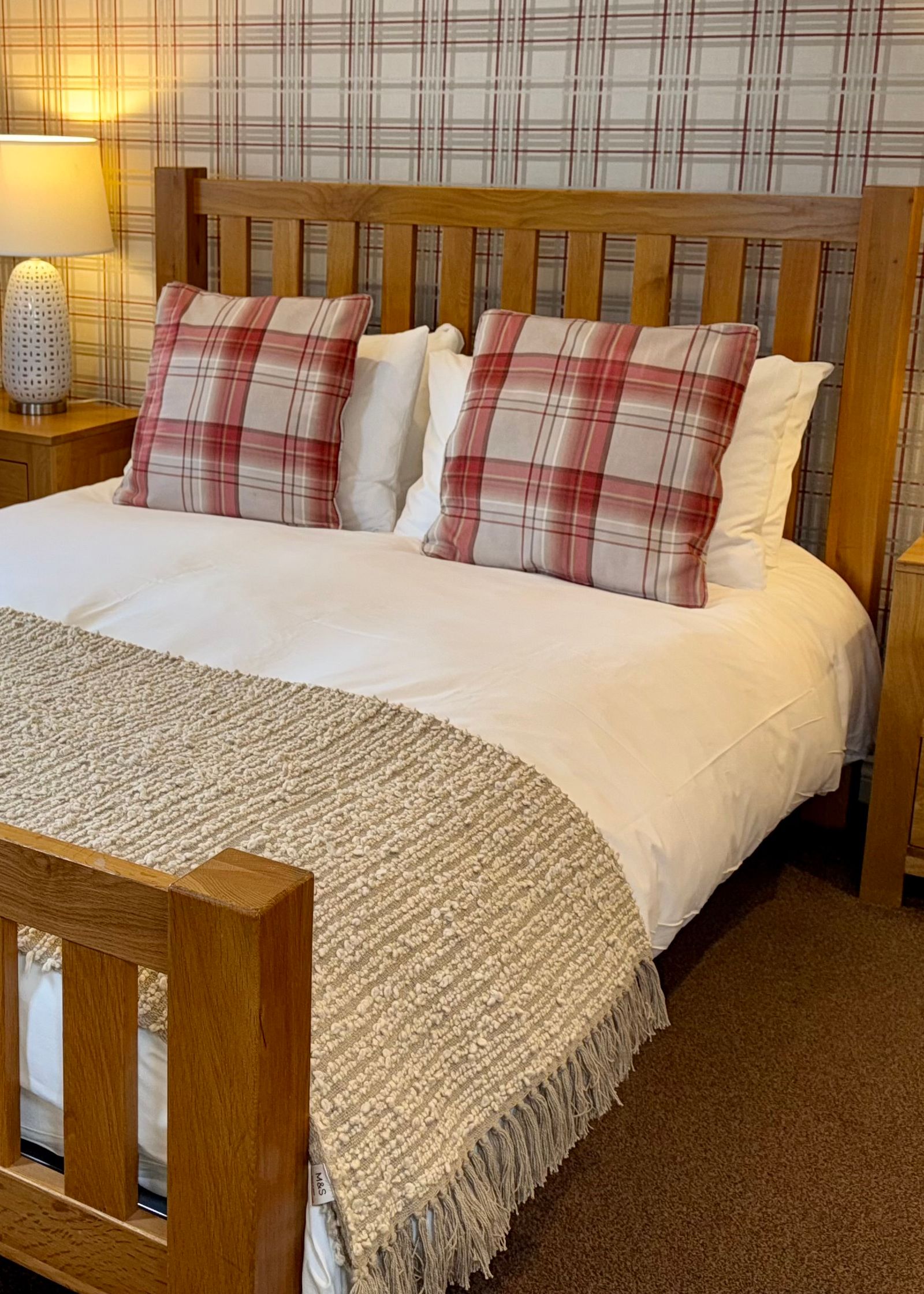 Cozy bedroom with wooden bed frame, plaid pillows, and bedside tables with lamps