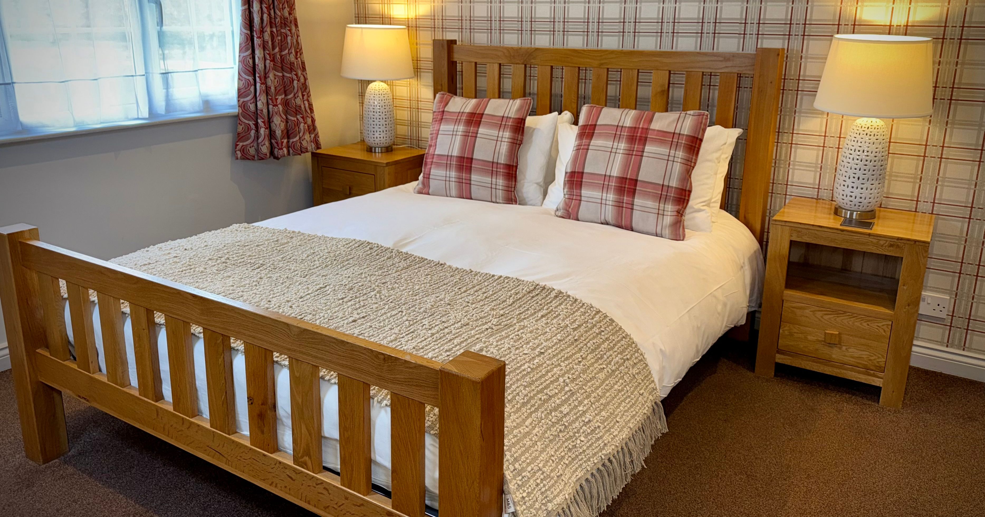 Cozy bedroom with wooden bed frame, plaid pillows, and bedside tables with lamps