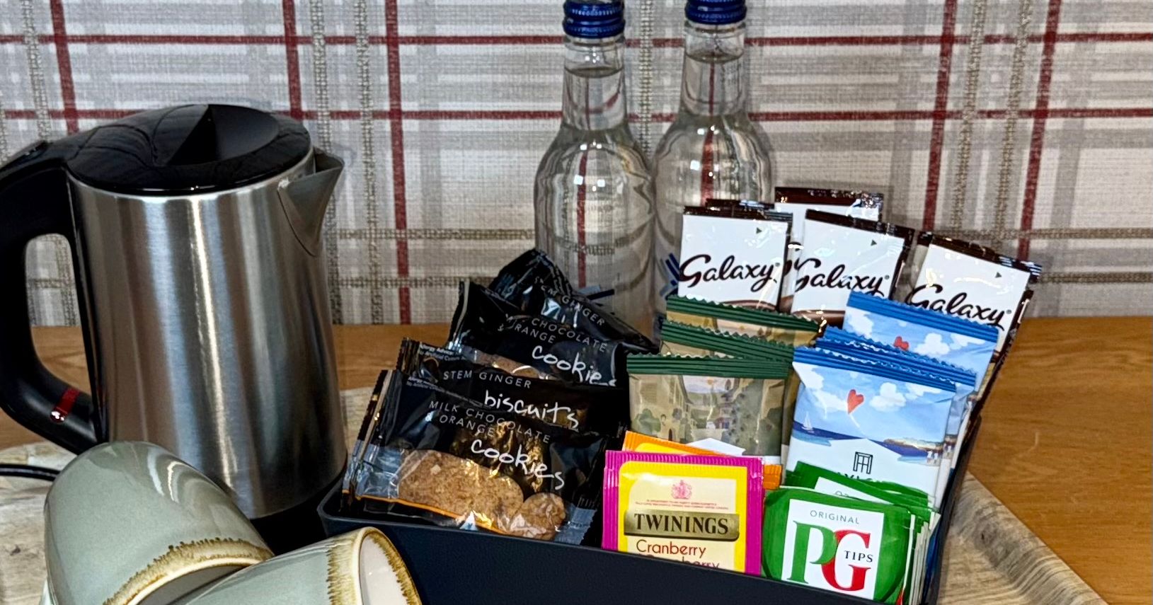 Hotel room refreshment tray with kettle, cups, water bottles, biscuits, instant drinks, and tea bags