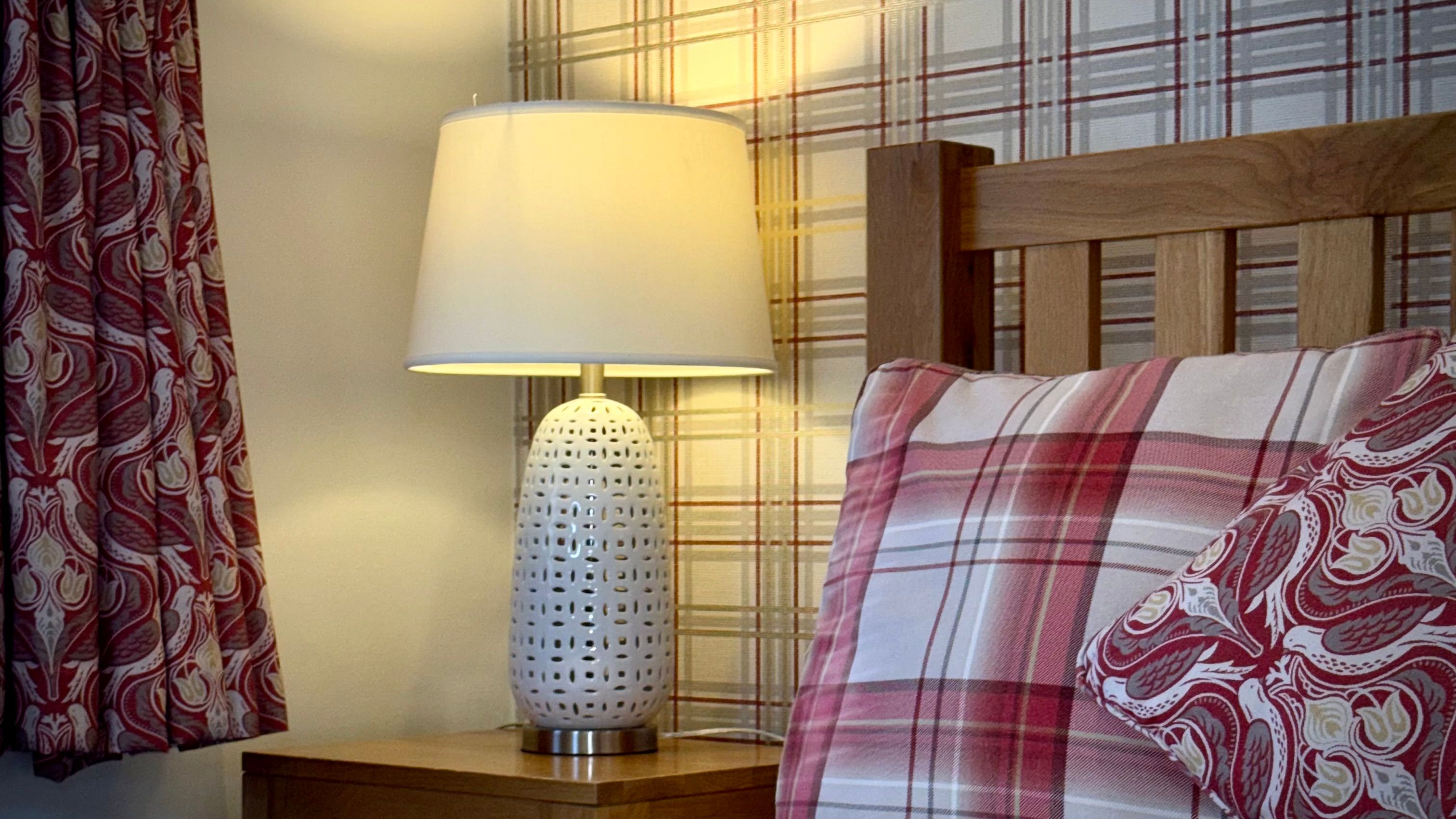 Cozy bedroom scene with a bedside lamp, plaid pillows, and patterned curtains