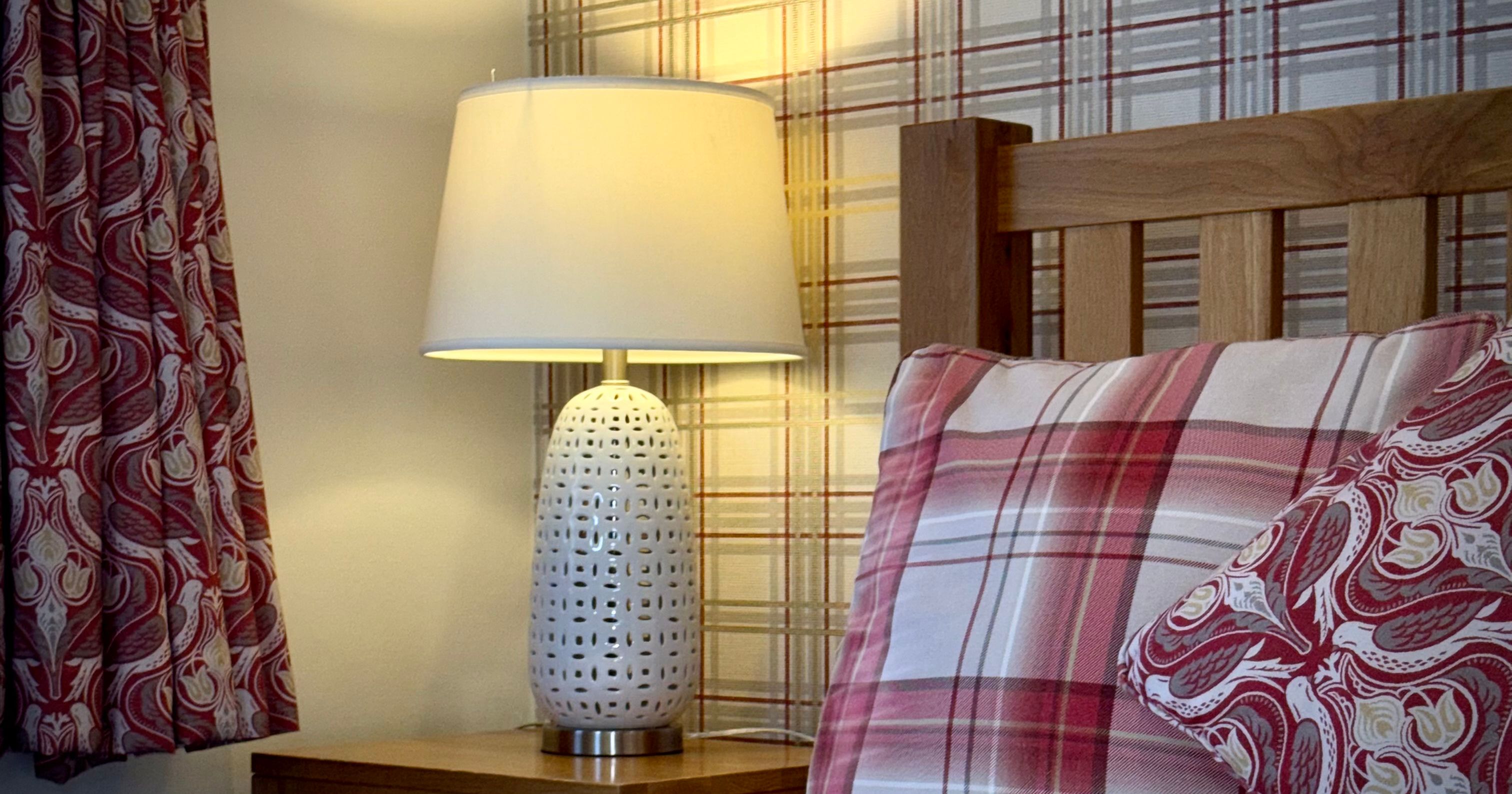 Cozy bedroom scene with a bedside lamp, plaid pillows, and patterned curtains