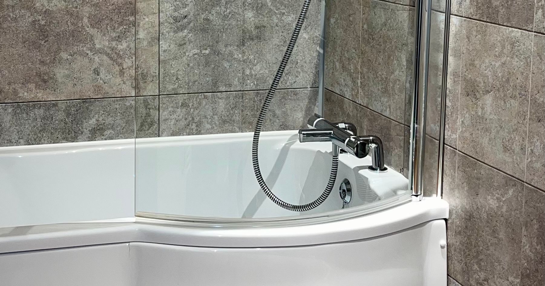 Modern bathroom with a curved white bathtub, glass shower screen, and gray tiled walls