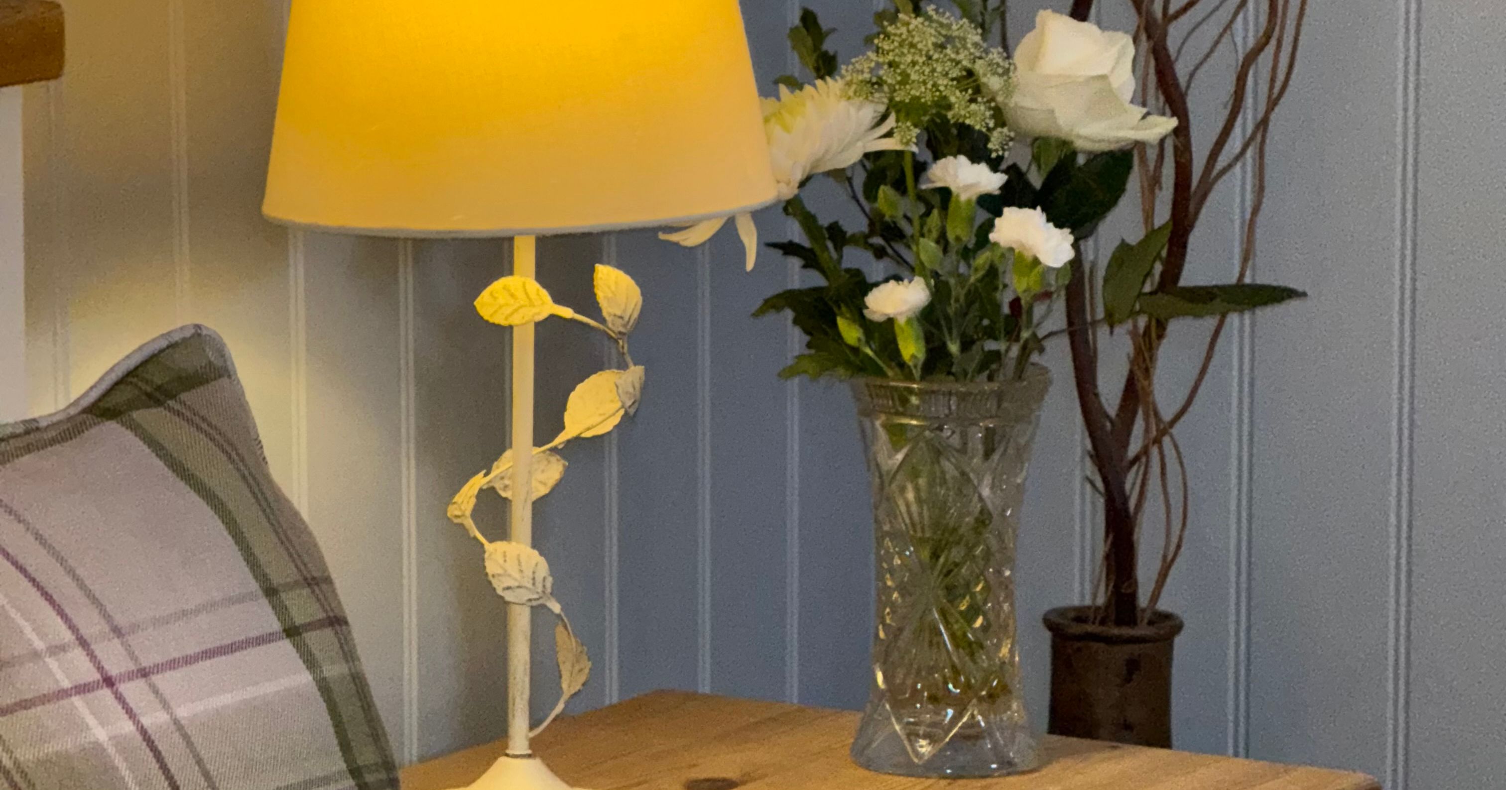 Bedside table with a lamp, flowers in a vase, and part of a pillow