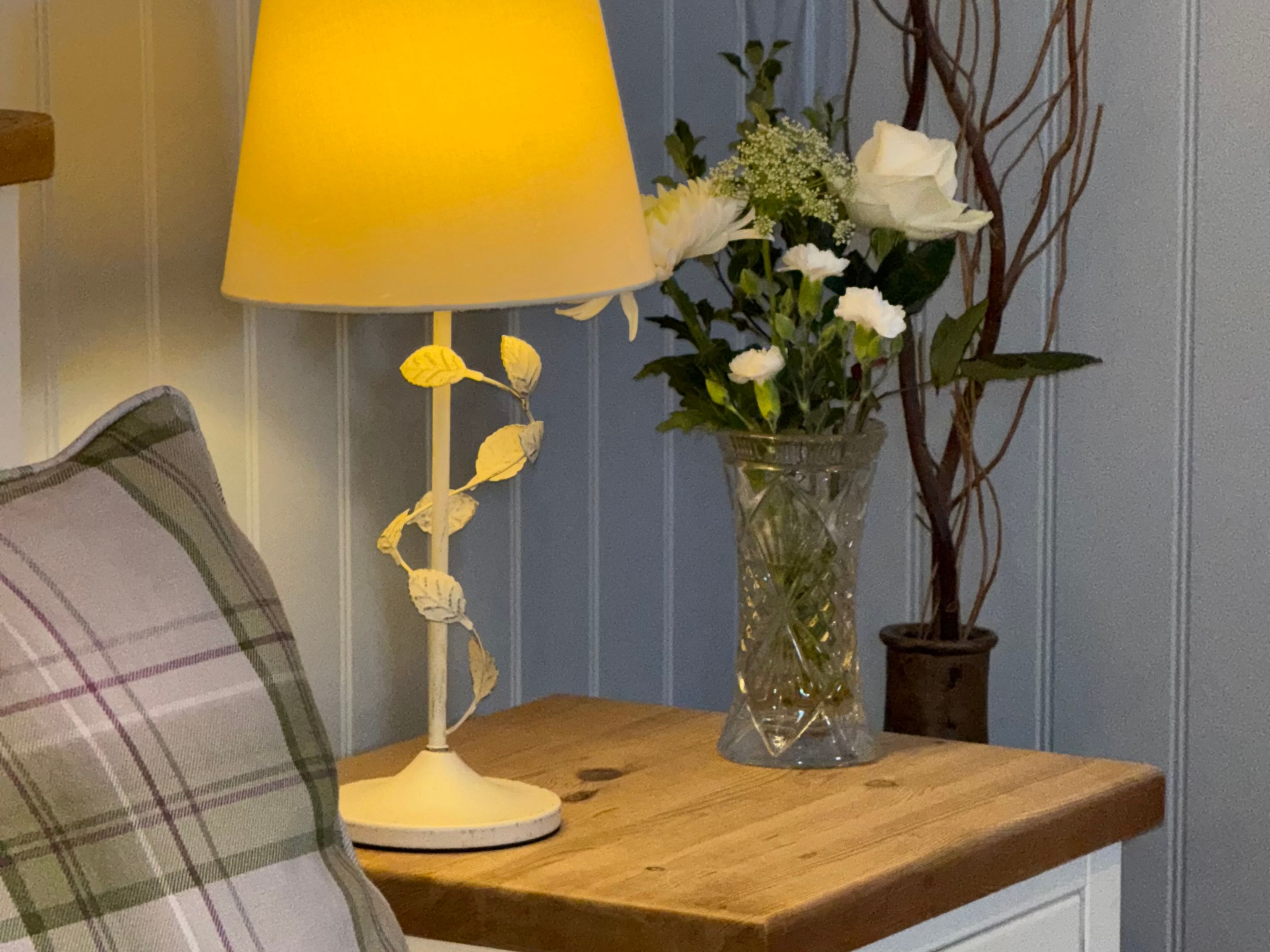 Bedside table with a lamp, flowers in a vase, and part of a pillow