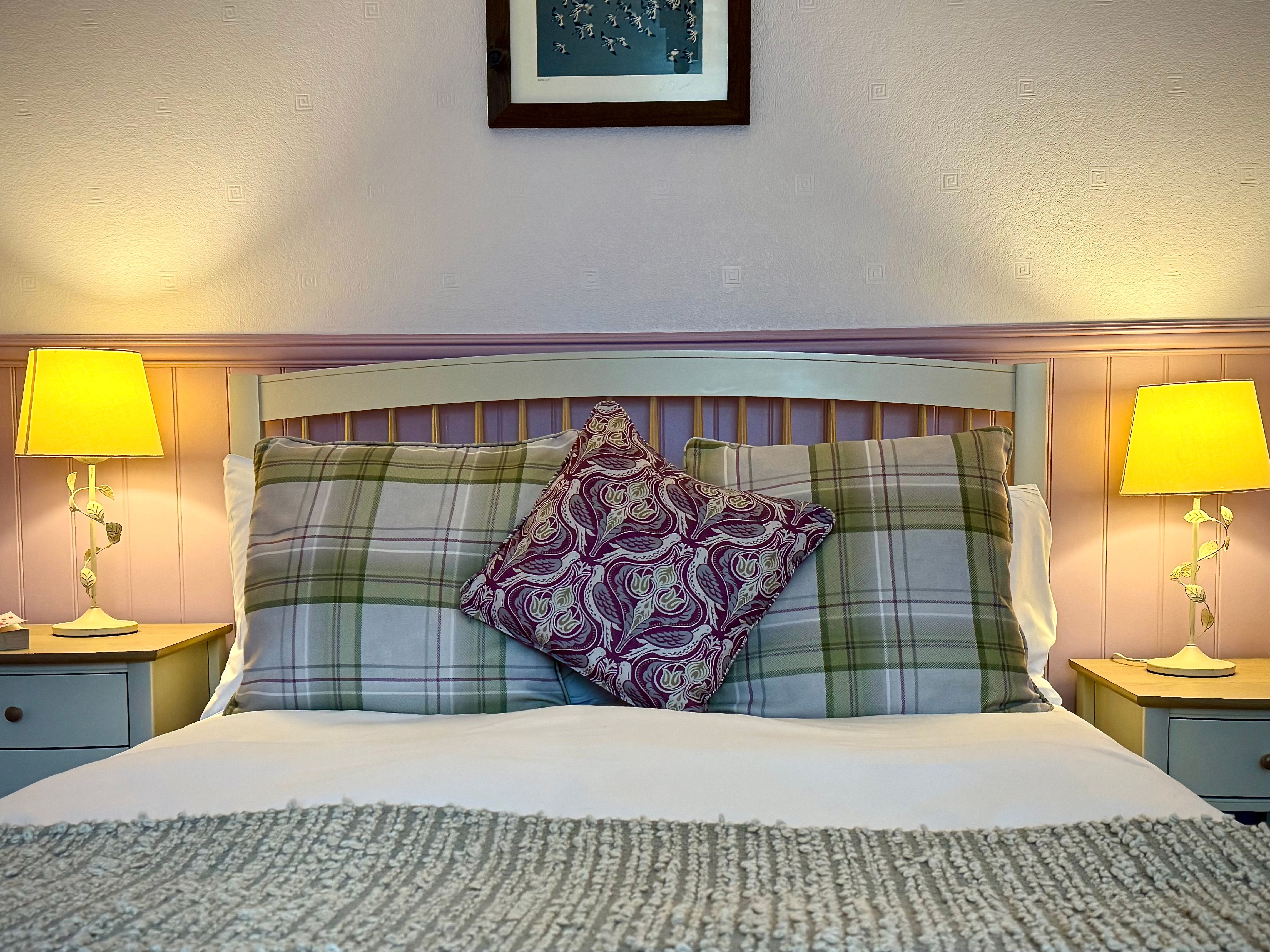 A cozy bedroom with plaid pillows, a patterned cushion, and two bedside lamps.