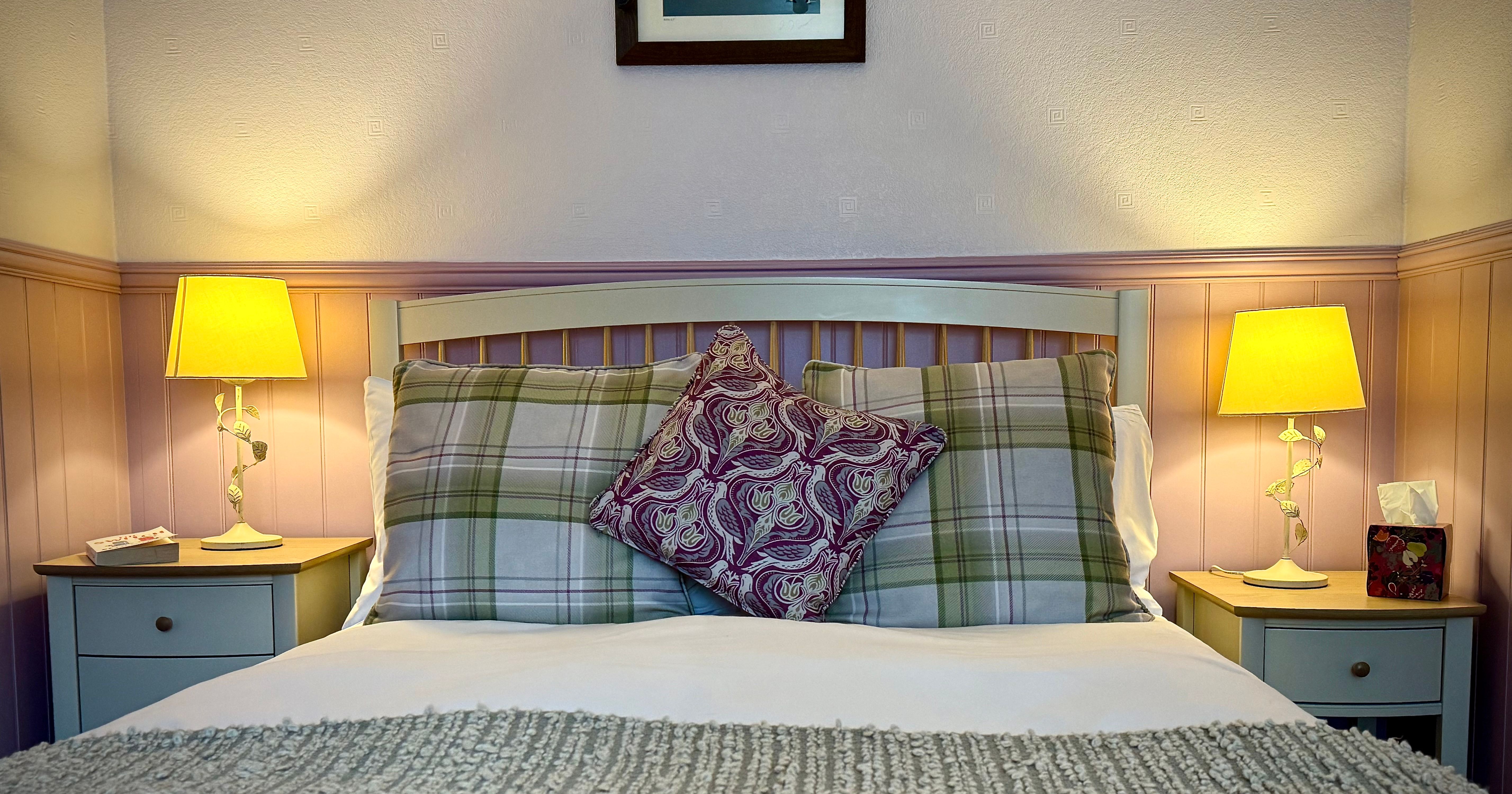 A cozy bedroom with plaid pillows, a patterned cushion, and two bedside lamps.
