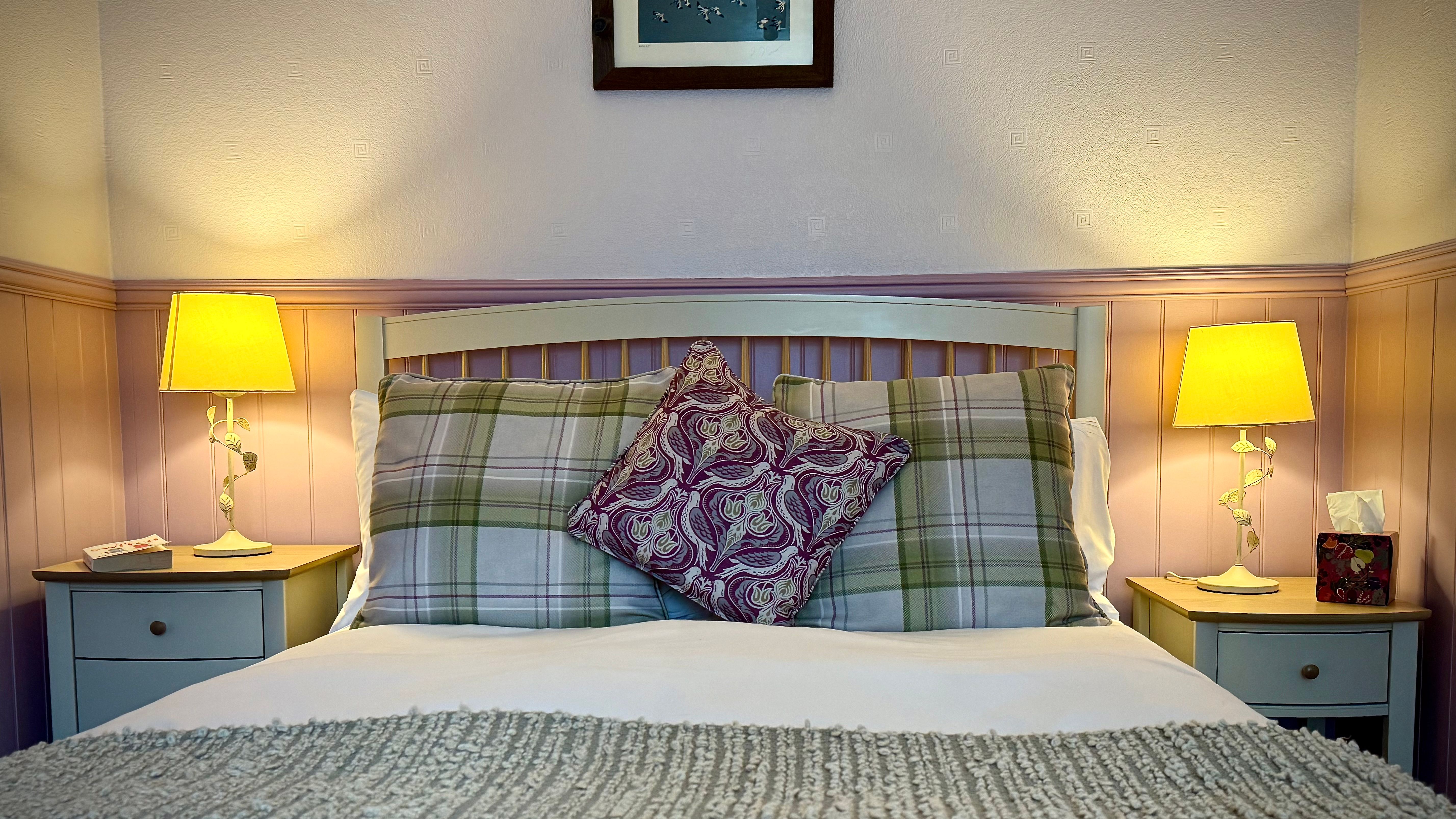 A cozy bedroom with plaid pillows, a patterned cushion, and two bedside lamps.