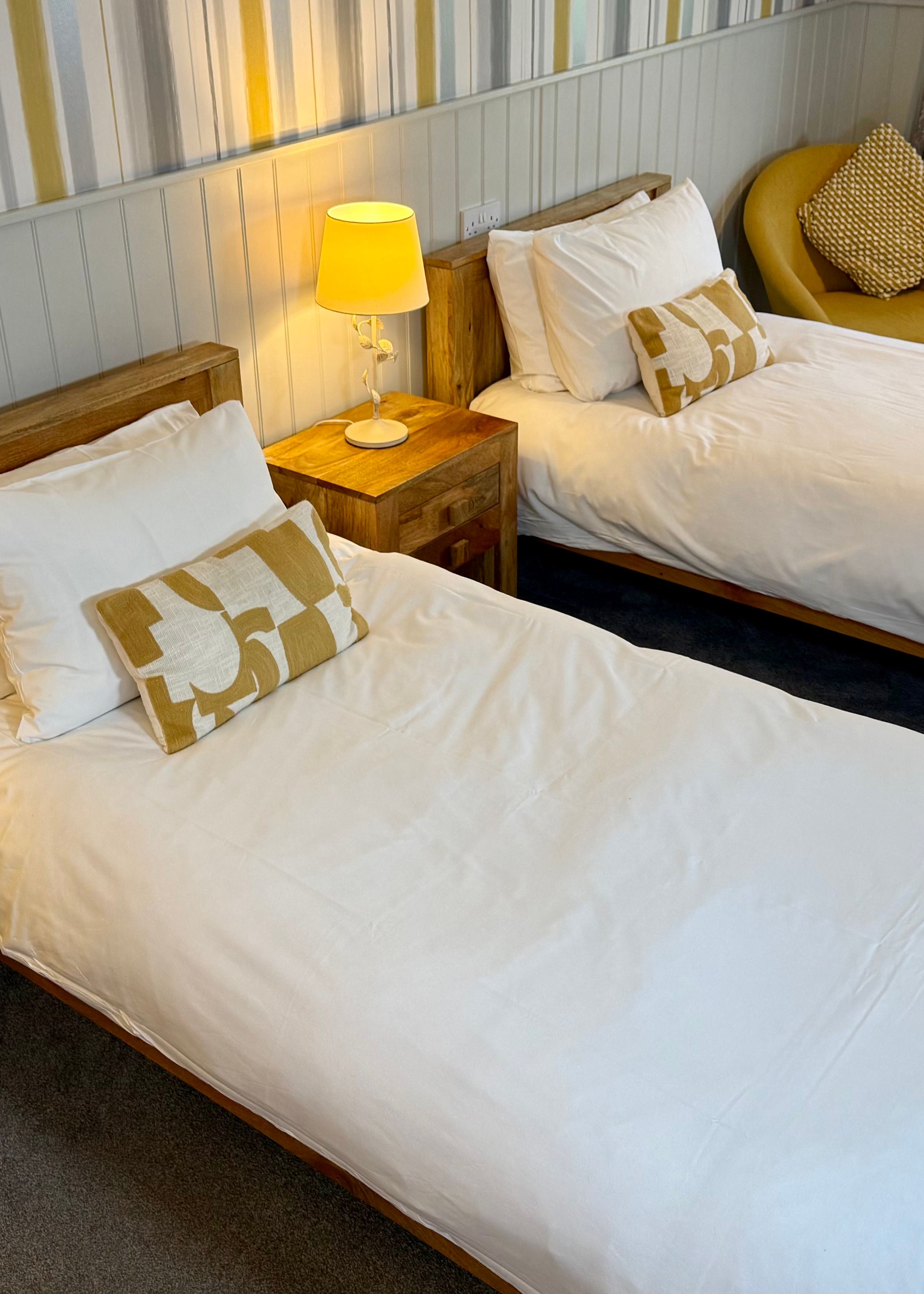Cozy twin bedroom with wooden beds, white bedding, matching nightstands, and warm yellow accents.