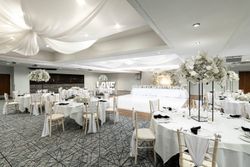 Elegant wedding reception hall decorated in white with round tables, floral centerpieces, draped ceiling, and a large 'LOVE' sign at the front.