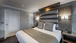 Modern hotel room with a large bed, two pillows, stylish headboard, bedside tables, wall-mounted lamps, and neutral-toned decor.