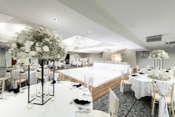 Elegant wedding reception hall decorated in white with floral centerpieces, round tables, a lighted dance floor, and a backdrop with large 'LOVE' letters.