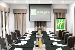 A modern conference room set up for a meeting with a long table, chairs, bottled drinks, glasses, notepads, pens, and a projector screen displaying the Holiday Inn logo.