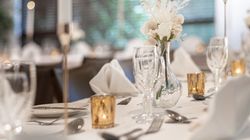 Elegant table setting with white flowers in a vase, tall candles, glassware, and gold votive holders