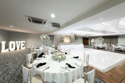 Elegant wedding reception hall with decorated round tables, floral centerpieces, white tablecloths, a lit-up dance floor, and large illuminated 'LOVE' letters in the background.