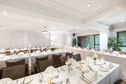 Elegantly decorated banquet hall with white tablecloths, neatly folded napkins, glassware, flowers, and candles set up for a formal event or wedding reception.