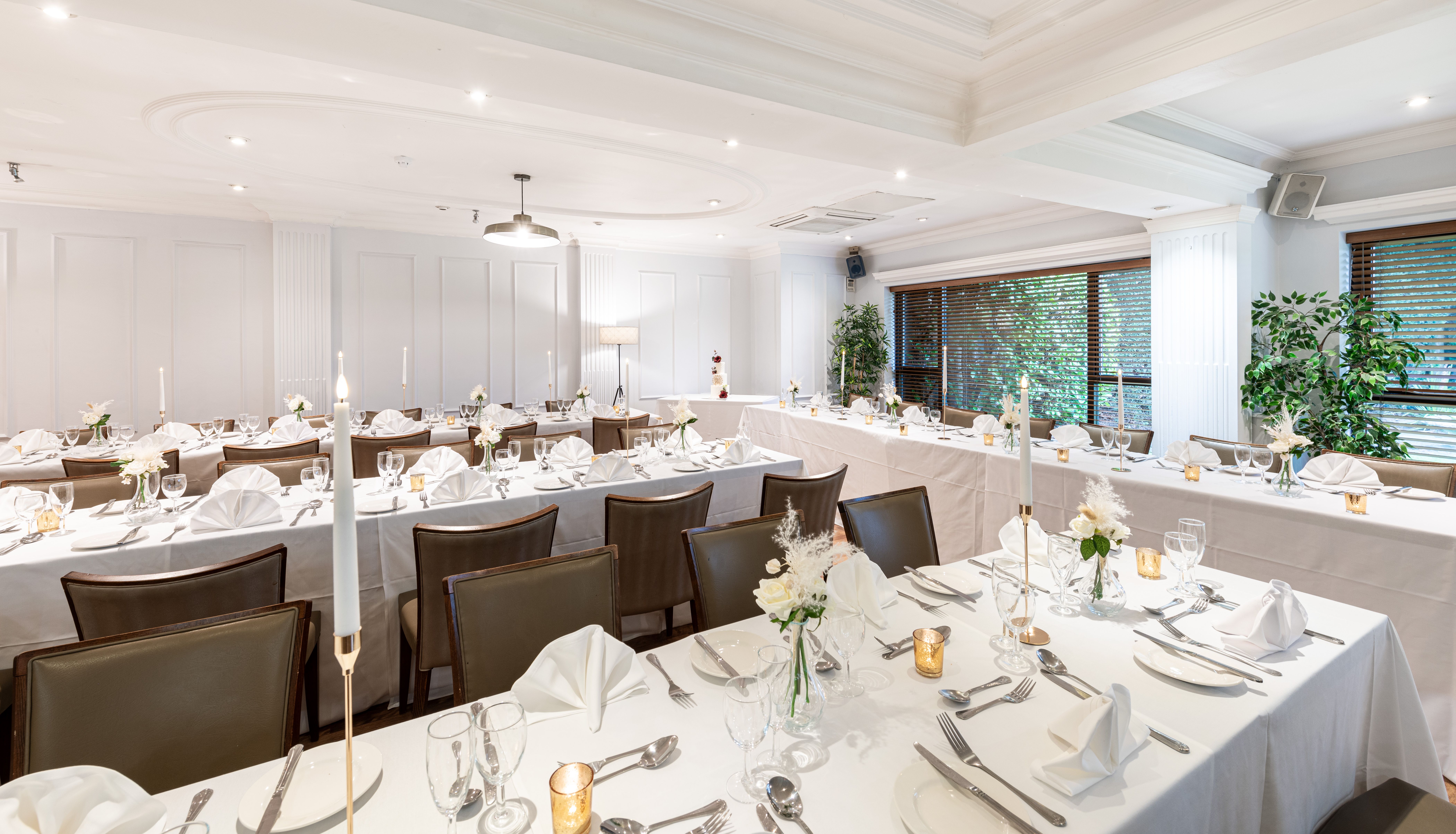 Elegantly decorated banquet hall with white tablecloths, neatly folded napkins, glassware, flowers, and candles set up for a formal event or wedding reception.