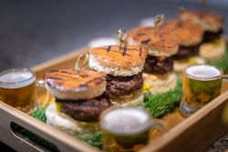 Mini burgers and small glasses of beer served on a wooden tray