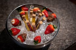 A metal bowl filled with ice, chocolate-dipped strawberries, fresh strawberries, and several glass test tubes with cork stoppers containing colorful liquids.