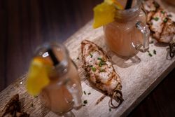 Grilled chicken skewers garnished with chopped chives served on a wooden board alongside mini mason jar glasses filled with a pink beverage, garnished with orange slices.