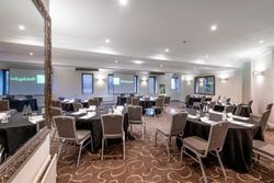 Spacious, modern conference room set up with round tables and chairs, black tablecloths, bottled water, notepads, and Holiday Inn branding visible on screens and banners.