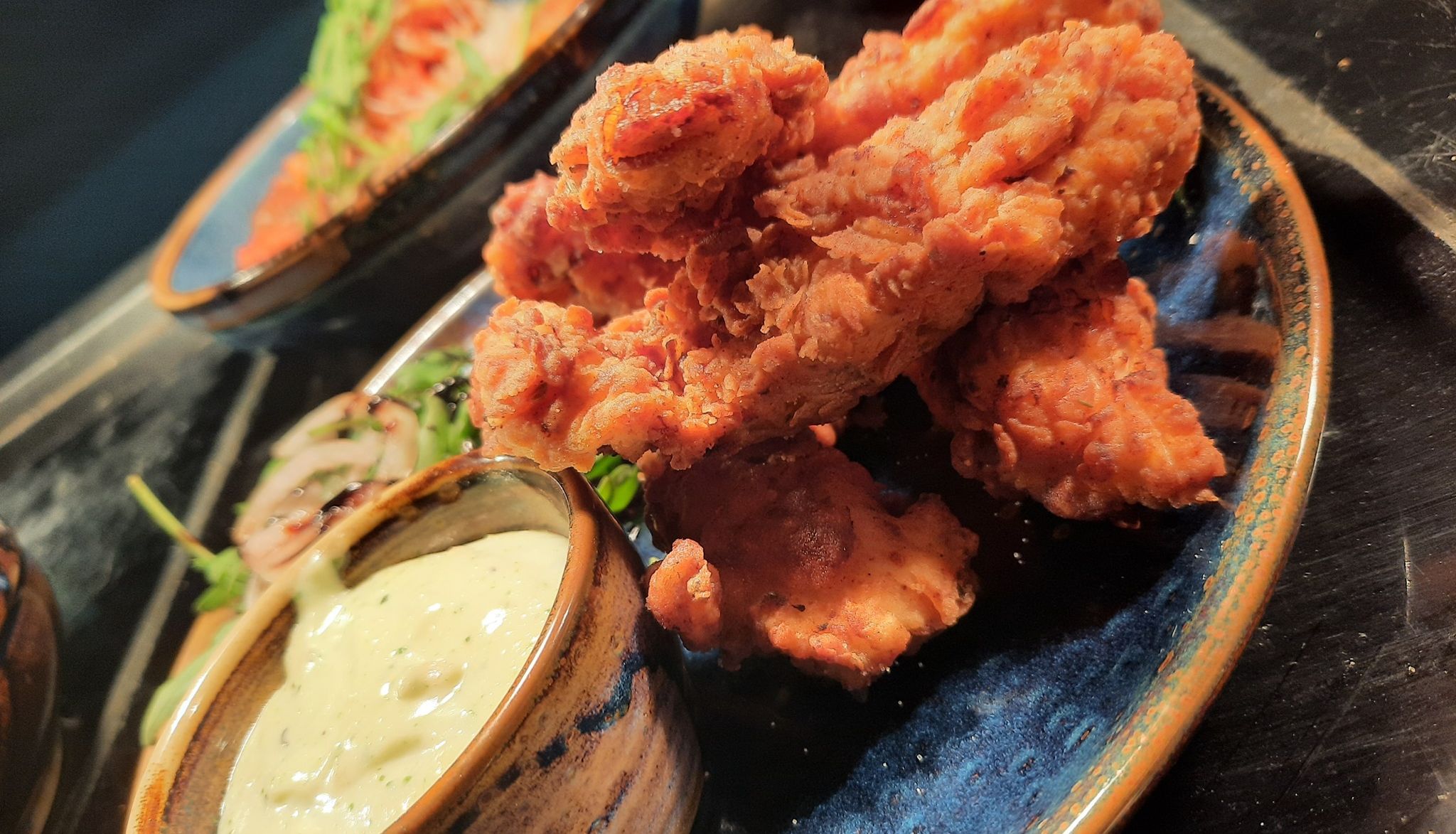 A plate of crispy fried chicken tenders served with a side of creamy dipping sauce.