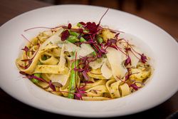 A plate of tagliatelle pasta with green beans, potato pieces, pesto sauce, parmesan cheese shavings, and microgreens garnish.