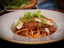 A plate of spaghetti bolognese topped with meat sauce, fresh herbs, and shaved parmesan cheese.