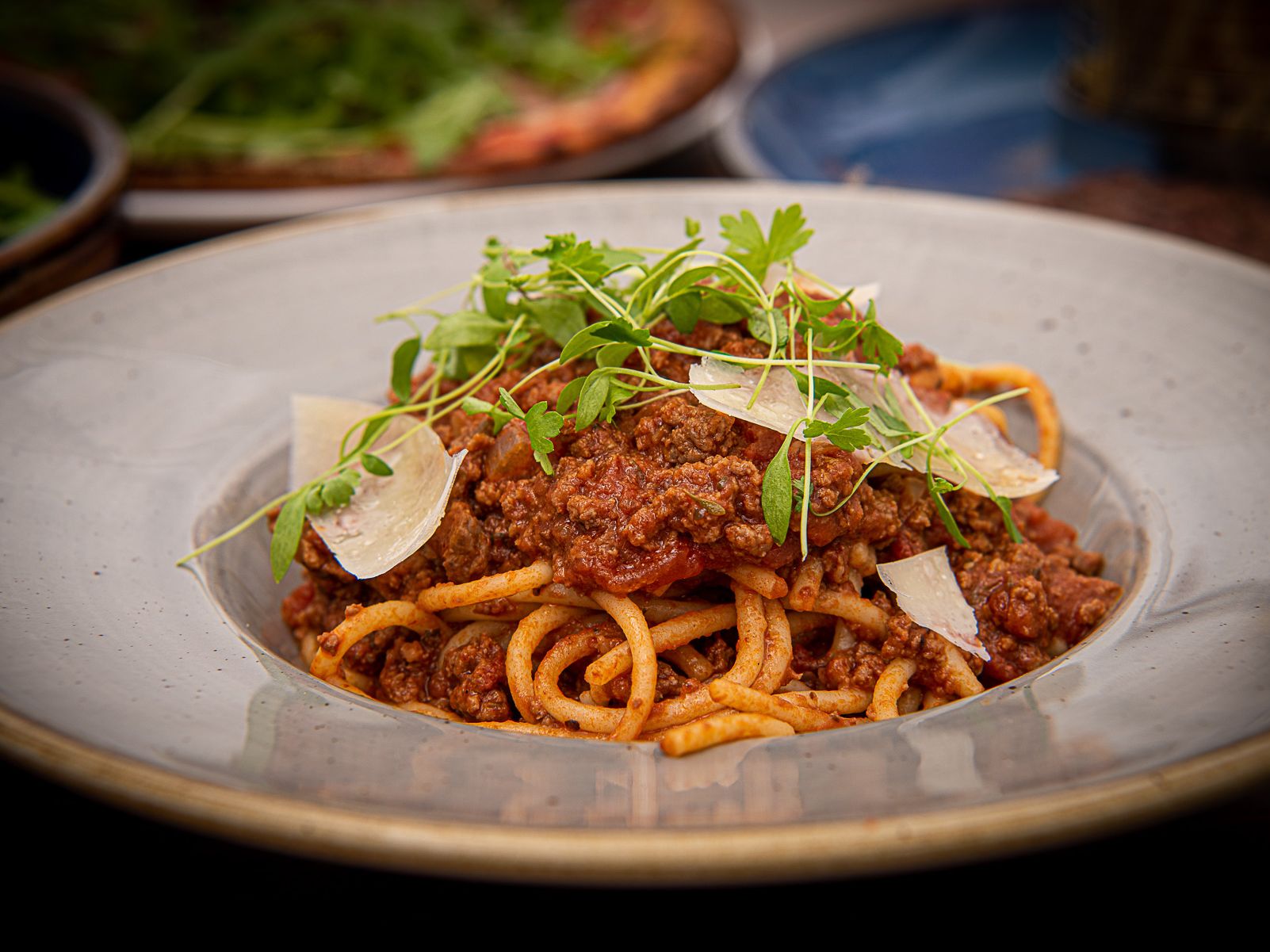 A plate of spaghetti bolognese topped with meat sauce, fresh herbs, and shaved parmesan cheese.