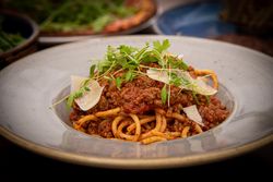 A plate of spaghetti bolognese topped with meat sauce, fresh herbs, and shaved parmesan cheese.