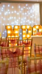 Decorated chairs with red bows facing illuminated letters and twinkling white lights backdrop