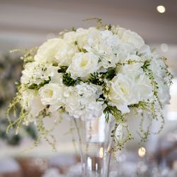 Elegant bouquet of white flowers, including roses and hydrangeas, arranged in a tall glass vase.