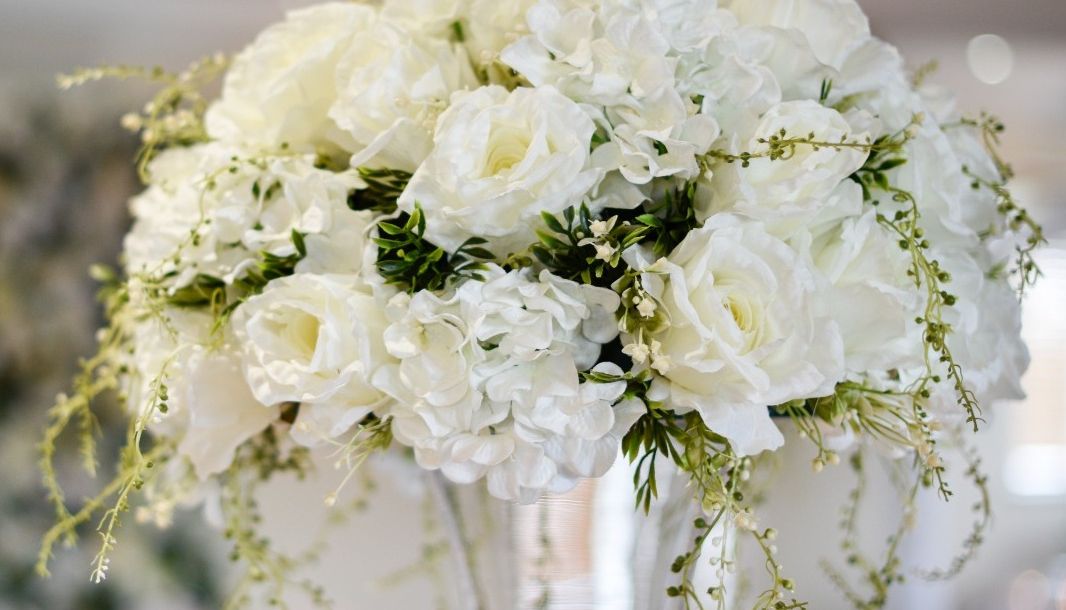 Elegant bouquet of white flowers, including roses and hydrangeas, arranged in a tall glass vase.