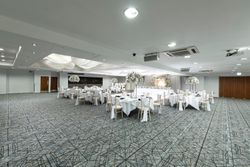 Spacious wedding reception hall with decorated round tables, white floral centerpieces, draped ceiling, and large illuminated 'LOVE' letters at the head table.