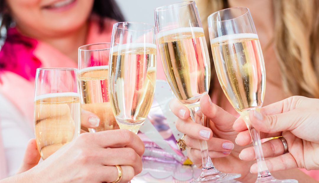 Group of women toasting with champagne glasses at a baby shower, holding a pink 'It's a Girl!' balloon.