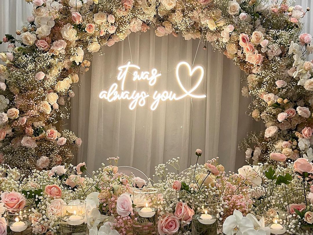 Romantic floral wedding arch and table arrangement with neon 'it was always you' sign