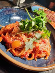 A bowl of spaghetti with tomato sauce, topped with shredded cheese and fresh arugula, served in a blue ceramic bowl.