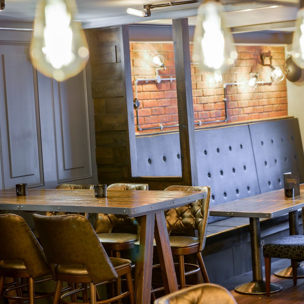 Cozy modern restaurant interior with wooden tables, leather chairs, exposed brick accent wall, and industrial-style light fixtures.